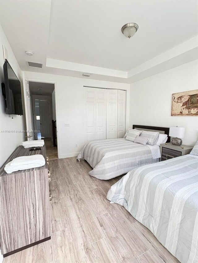 bedroom featuring a raised ceiling, wood finished floors, baseboards, and a closet