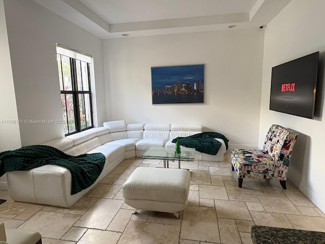 living room with a tray ceiling, stone tile flooring, and baseboards