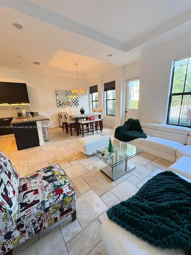 living room featuring a raised ceiling, stone tile floors, a chandelier, and recessed lighting