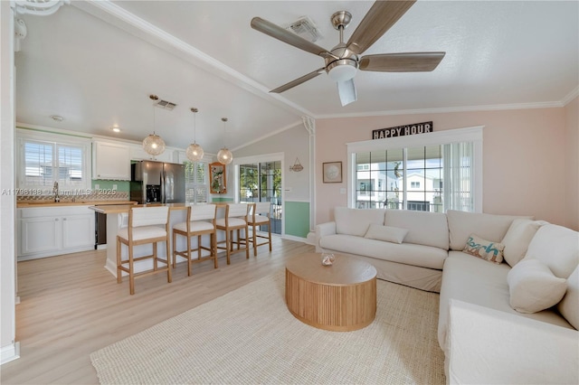 living room featuring light wood-type flooring, vaulted ceiling, crown molding, ceiling fan, and baseboards