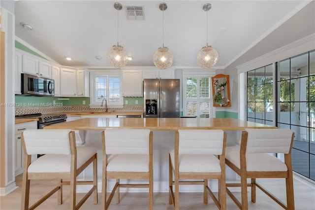 kitchen featuring appliances with stainless steel finishes, ornamental molding, lofted ceiling, white cabinetry, and a sink