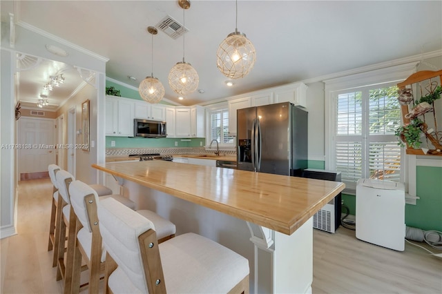 kitchen with stainless steel appliances, ornamental molding, light wood finished floors, white cabinetry, and butcher block counters