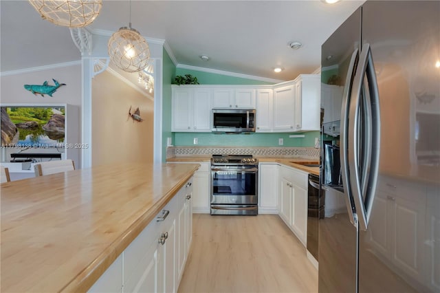 kitchen with appliances with stainless steel finishes, ornamental molding, wood counters, white cabinetry, and vaulted ceiling