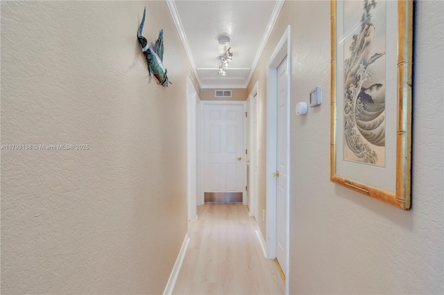 corridor with ornamental molding, light wood-style flooring, baseboards, and a textured wall