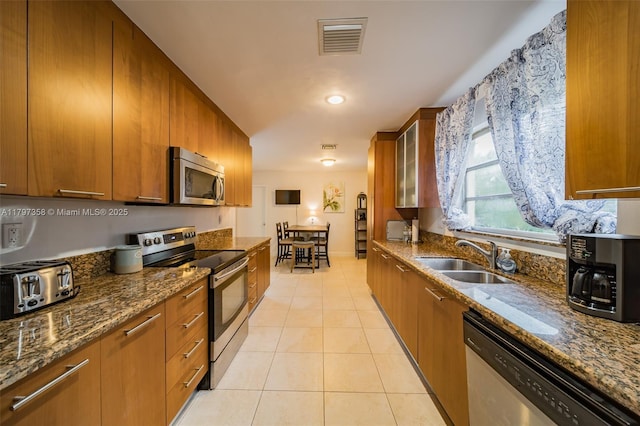 4410 N Buchanan St, Hollywood, FL 33021 - kitchen with appliances with stainless steel finishes, a sink, brown cabinets, light tile patterned floors, and dark stone countertops