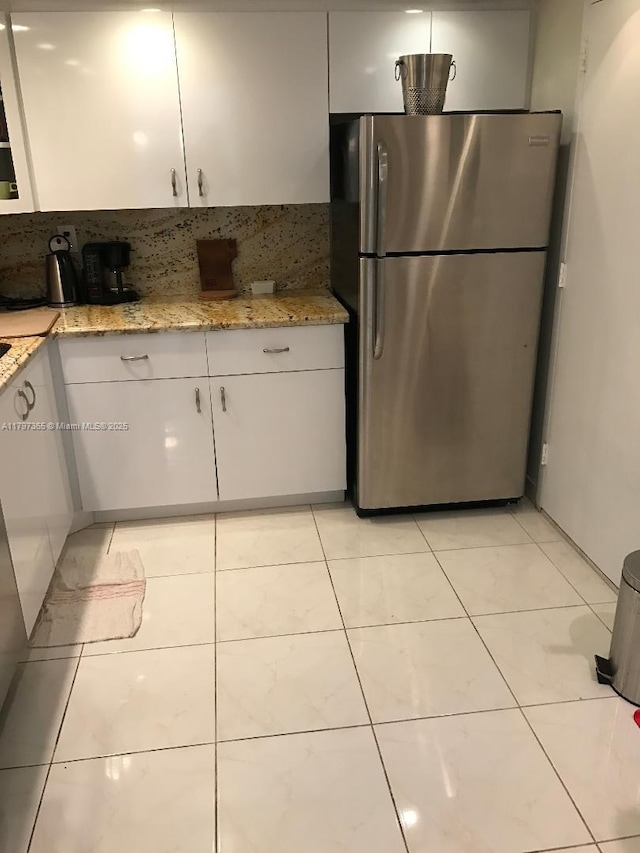 kitchen with freestanding refrigerator, white cabinetry, and decorative backsplash