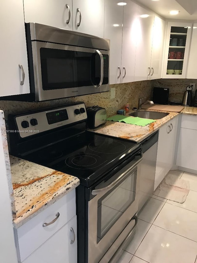 kitchen with appliances with stainless steel finishes, white cabinets, a sink, backsplash, and glass insert cabinets