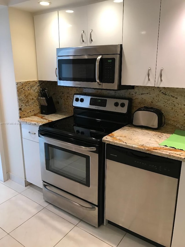 kitchen with appliances with stainless steel finishes, white cabinets, tasteful backsplash, light tile patterned flooring, and light stone counters