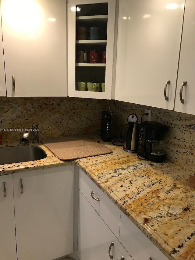 kitchen featuring a sink, white cabinetry, decorative backsplash, and light stone counters