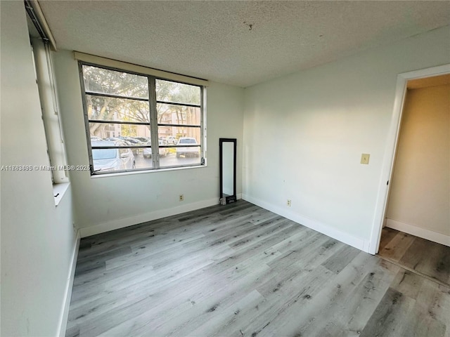 spare room with a textured ceiling, wood finished floors, and baseboards