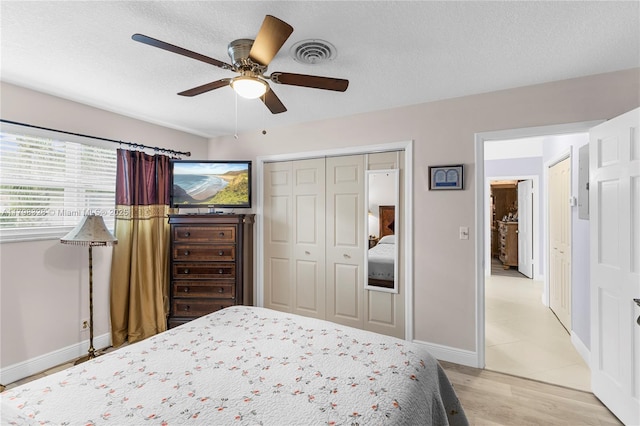 bedroom with light wood-style floors, a ceiling fan, a closet, baseboards, and a textured ceiling