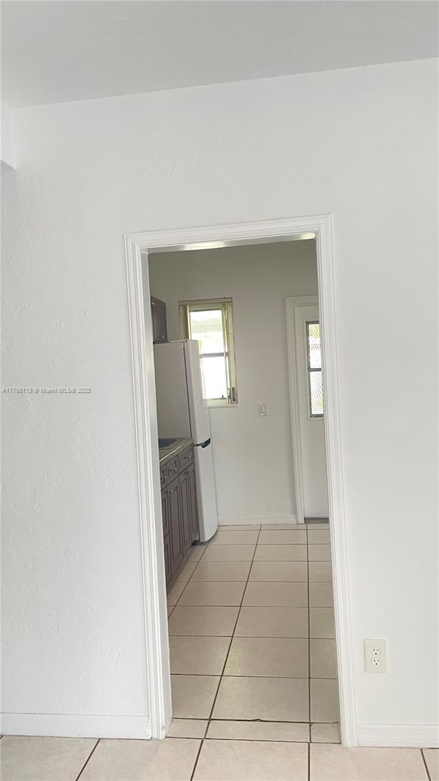 hall featuring light tile patterned floors and baseboards