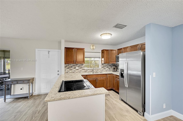 14030 Nesting Way Unit D, Delray Beach, FL 33484 - kitchen featuring appliances with stainless steel finishes, brown cabinetry, light wood-style flooring, a peninsula, and a textured ceiling