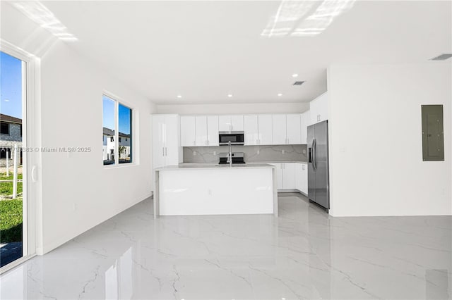 kitchen with appliances with stainless steel finishes, electric panel, light marble finish floors, white cabinetry, and an island with sink
