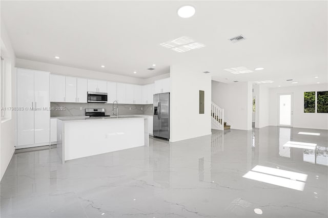 kitchen featuring stainless steel appliances, light marble finish floors, white cabinetry, light countertops, and open floor plan