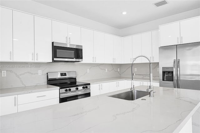 kitchen with appliances with stainless steel finishes, a sink, white cabinets, backsplash, and light stone countertops