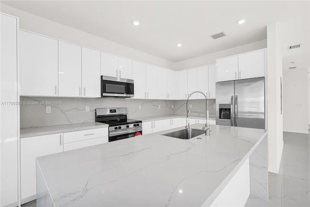 kitchen featuring appliances with stainless steel finishes, a sink, a kitchen island with sink, white cabinets, and recessed lighting