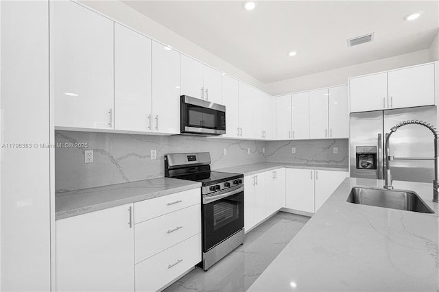 kitchen with appliances with stainless steel finishes, light marble finish flooring, light stone countertops, a sink, and recessed lighting