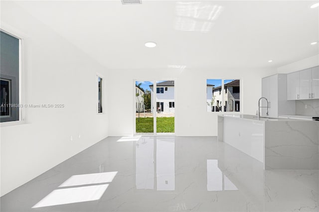 unfurnished living room with light marble finish floors, a sink, and recessed lighting