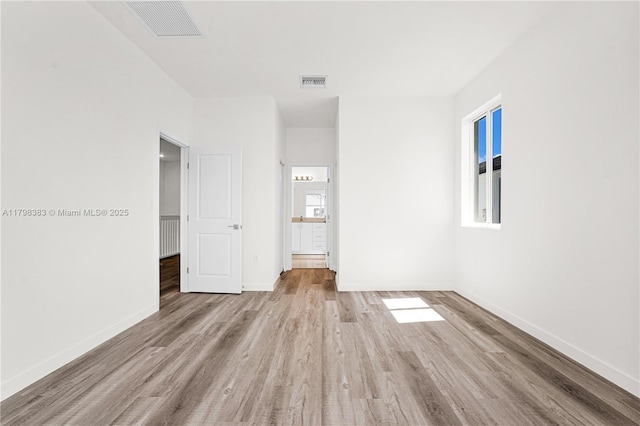 unfurnished bedroom with wood finished floors, baseboards, and ensuite bathroom