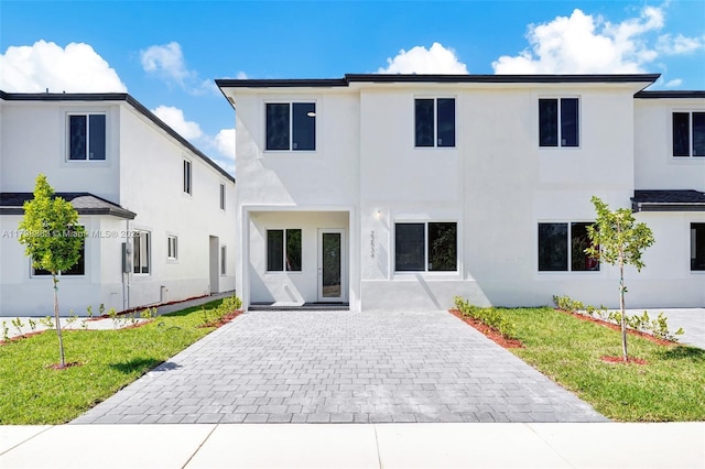 view of front of property featuring stucco siding, decorative driveway, and a front yard