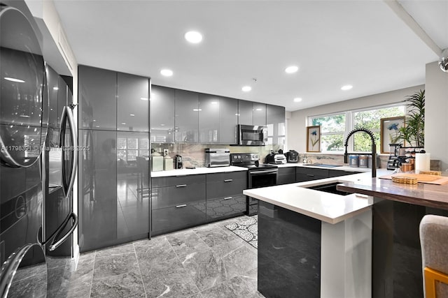 kitchen featuring stainless steel appliances, gray cabinetry, a sink, modern cabinets, and a peninsula