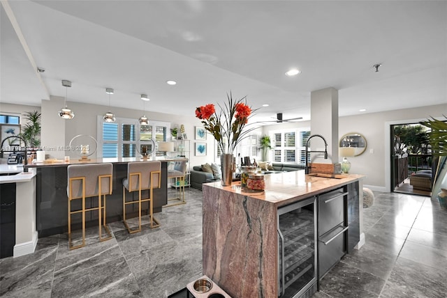 kitchen with wine cooler, a kitchen island with sink, plenty of natural light, a sink, and recessed lighting