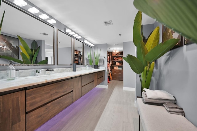 full bathroom with wood finished floors, double vanity, a walk in closet, and baseboards