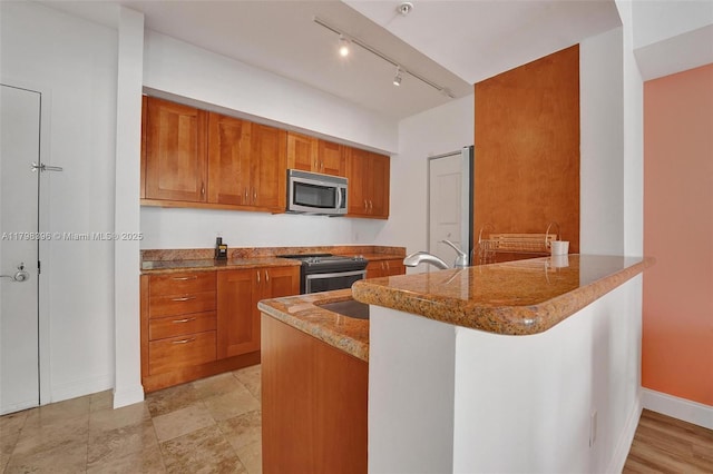 kitchen featuring stainless steel appliances, brown cabinetry, a peninsula, and baseboards
