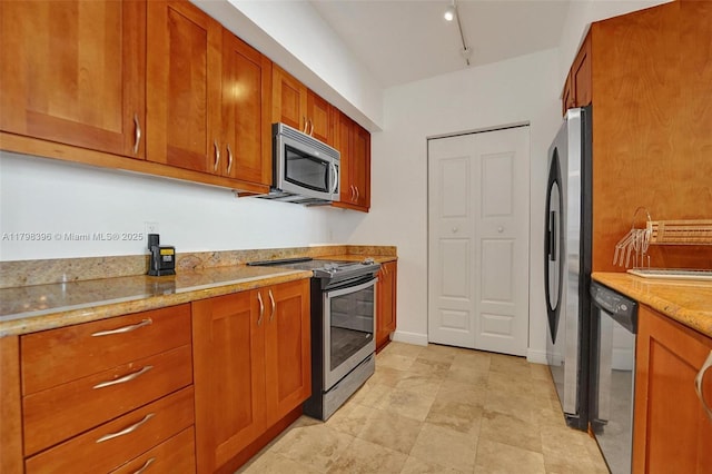kitchen with appliances with stainless steel finishes, brown cabinets, light stone countertops, and track lighting