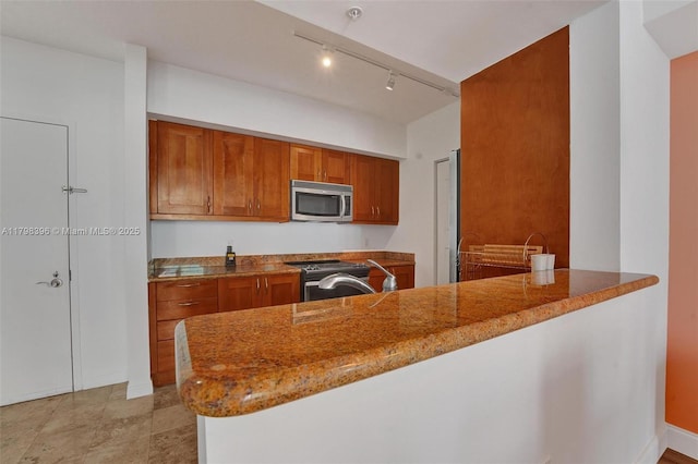 kitchen with appliances with stainless steel finishes, brown cabinetry, a peninsula, and stone counters
