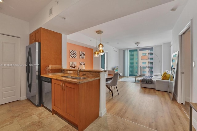 kitchen with a sink, appliances with stainless steel finishes, brown cabinetry, open floor plan, and a peninsula