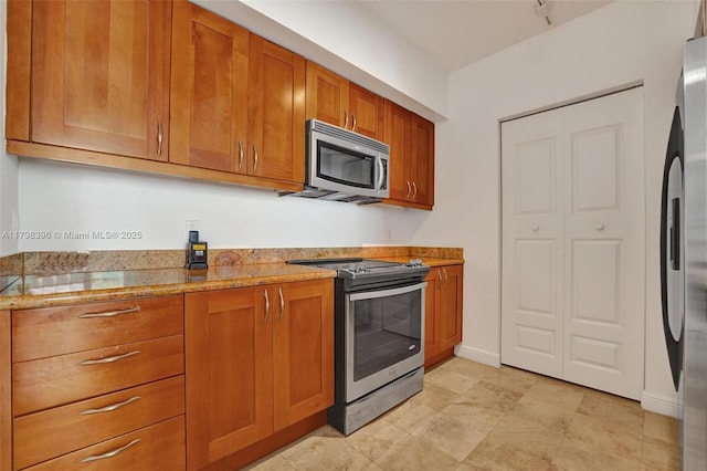 kitchen featuring appliances with stainless steel finishes, brown cabinetry, light stone countertops, and baseboards