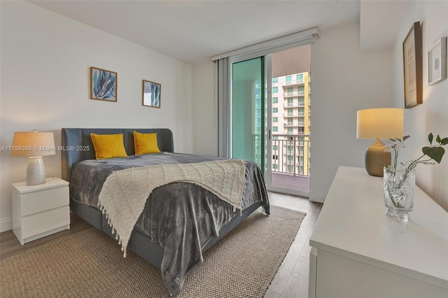 bedroom with light wood-style floors, access to exterior, expansive windows, and baseboards