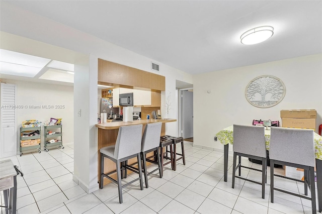kitchen with black microwave, light tile patterned flooring, a breakfast bar area, and freestanding refrigerator