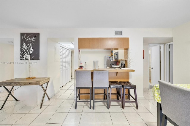 kitchen with freestanding refrigerator, a breakfast bar, light tile patterned flooring, and light countertops