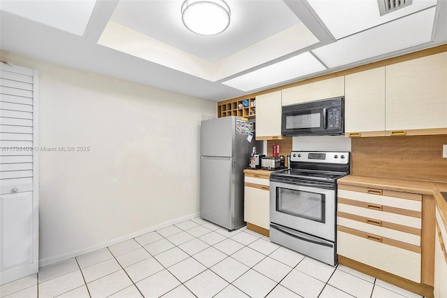kitchen featuring appliances with stainless steel finishes, baseboards, light countertops, cream cabinetry, and a tray ceiling