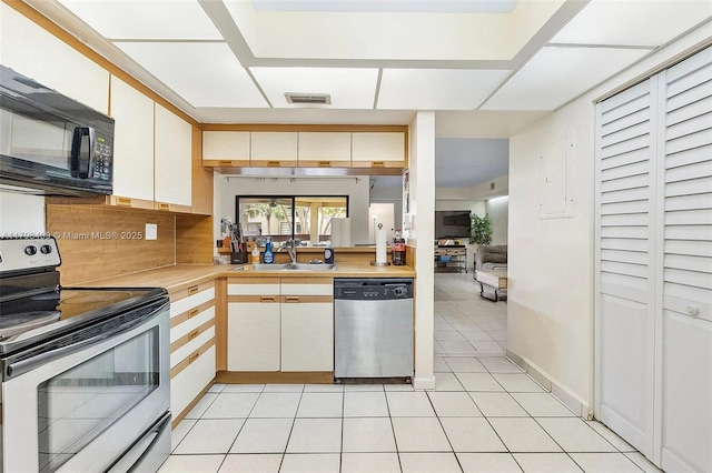 kitchen featuring appliances with stainless steel finishes, a sink, light countertops, light tile patterned floors, and white cabinetry