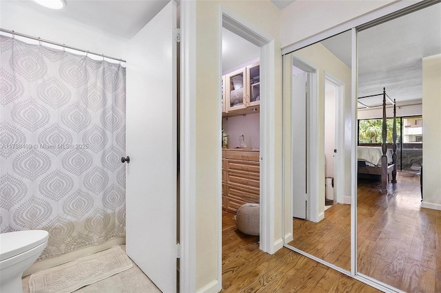 ensuite bathroom featuring toilet, wood finished floors, and a shower with curtain