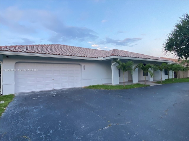 view of front of property with driveway, a tile roof, a garage, and stucco siding