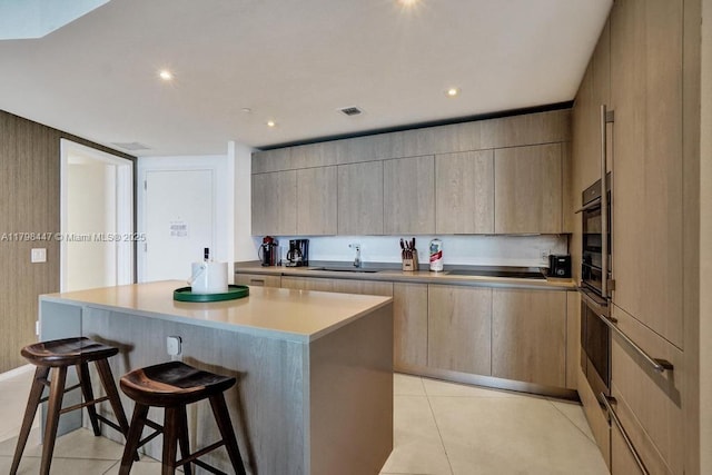 kitchen with a sink, a kitchen bar, modern cabinets, light brown cabinets, and recessed lighting