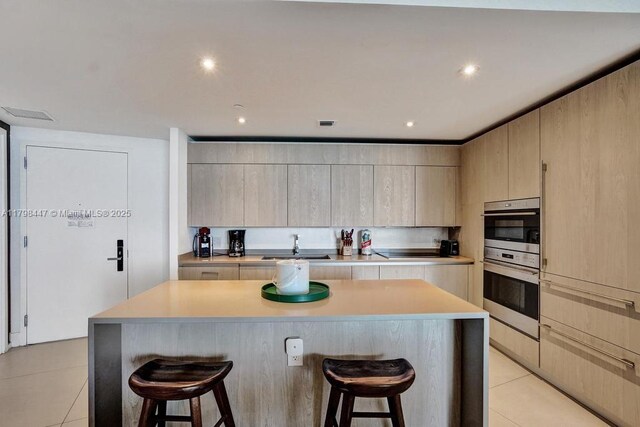 kitchen with a kitchen bar, a sink, light countertops, stainless steel double oven, and recessed lighting
