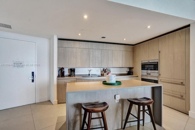 kitchen featuring a breakfast bar, stainless steel double oven, a sink, a kitchen island, and recessed lighting
