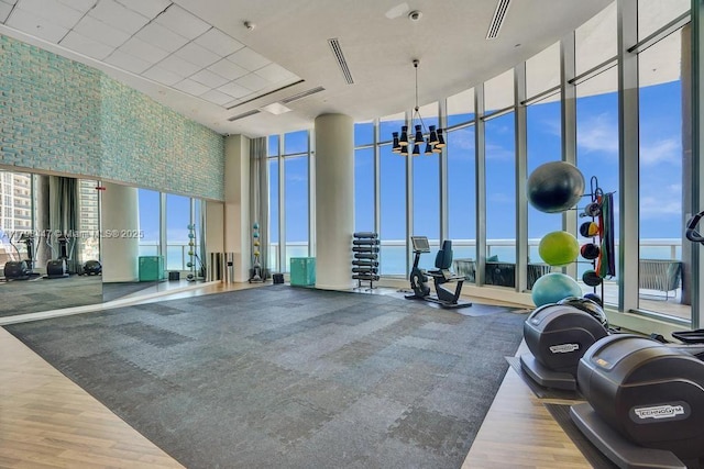 exercise room with expansive windows, wood finished floors, a towering ceiling, plenty of natural light, and a chandelier