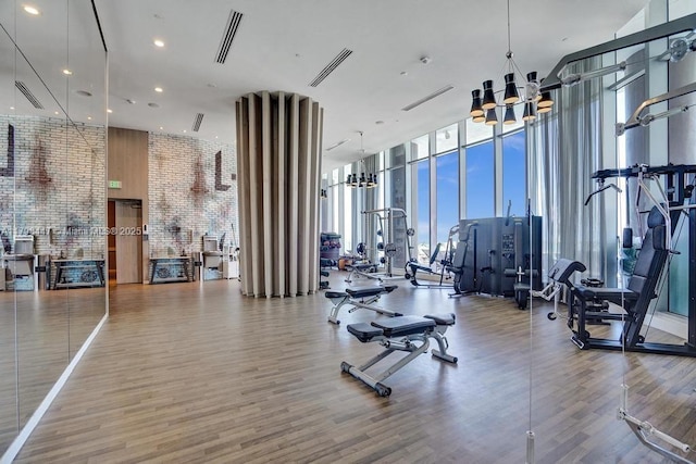 workout area featuring a wall of windows, a high ceiling, a chandelier, wood finished floors, and recessed lighting