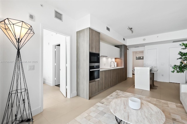 kitchen with oven, modern cabinets, light countertops, black microwave, and a sink
