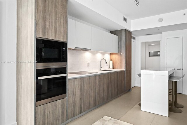 kitchen with black appliances, modern cabinets, a sink, and tasteful backsplash