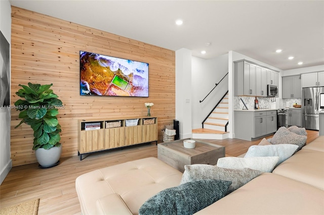 living room featuring recessed lighting, stairway, light wood-style flooring, wooden walls, and baseboards