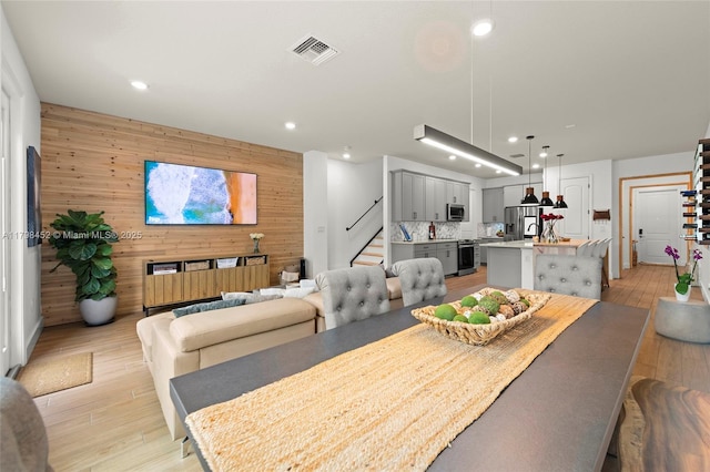 dining room featuring stairs, recessed lighting, light wood-type flooring, and wood walls