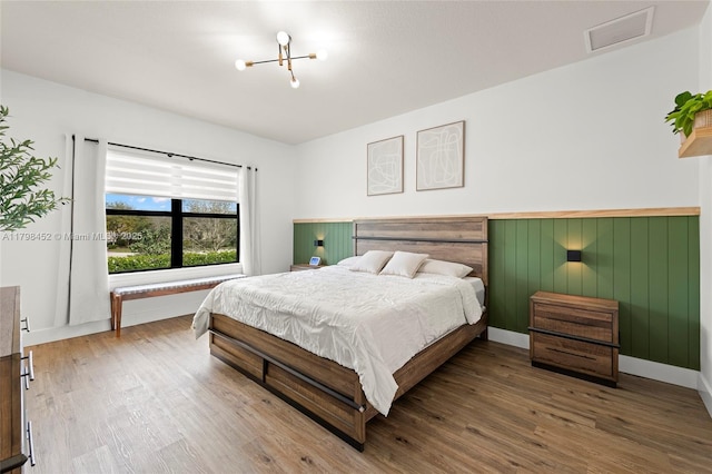 bedroom with wood finished floors, a chandelier, wainscoting, and baseboards